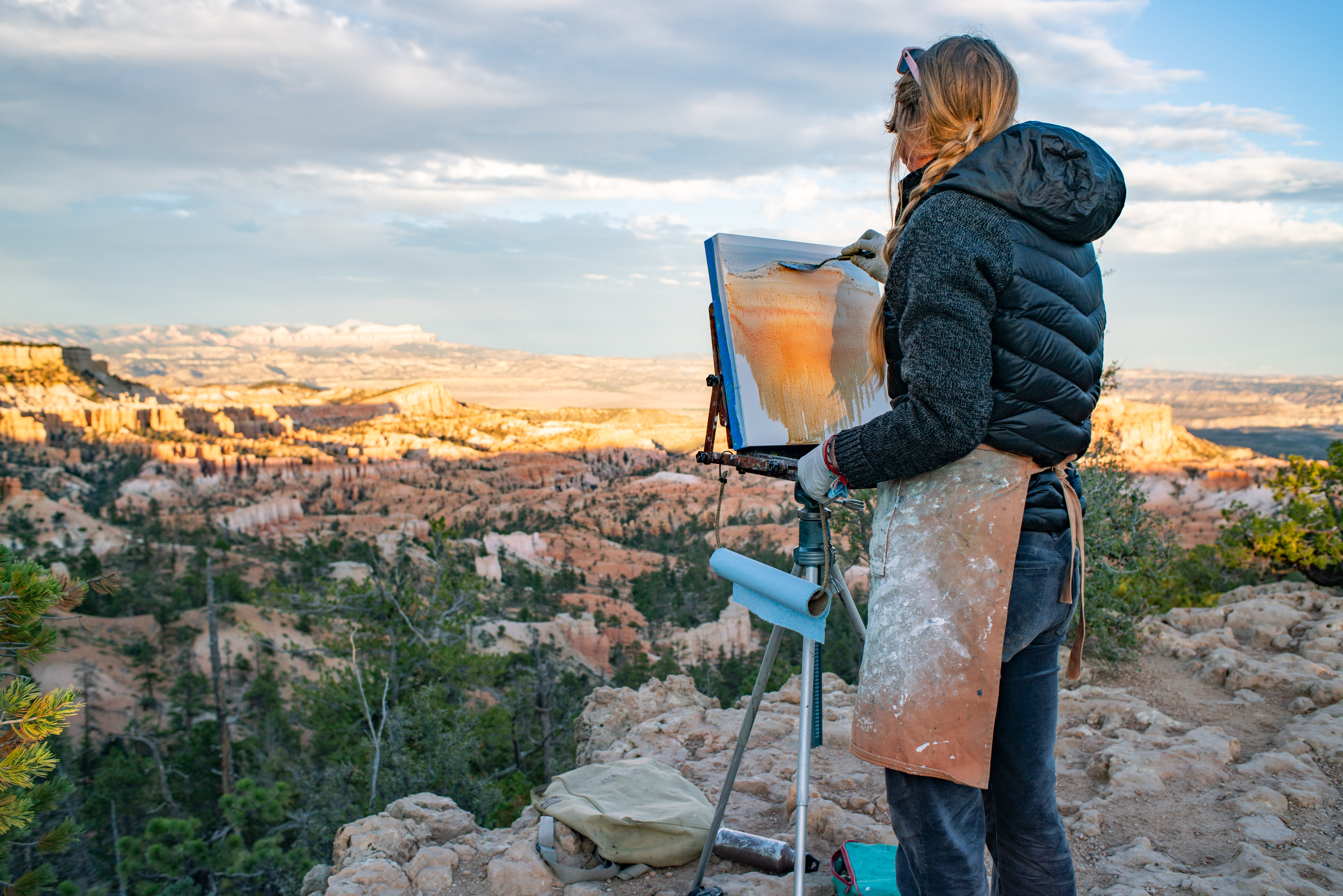 An artist stands at an easel painting a red rock landscape
