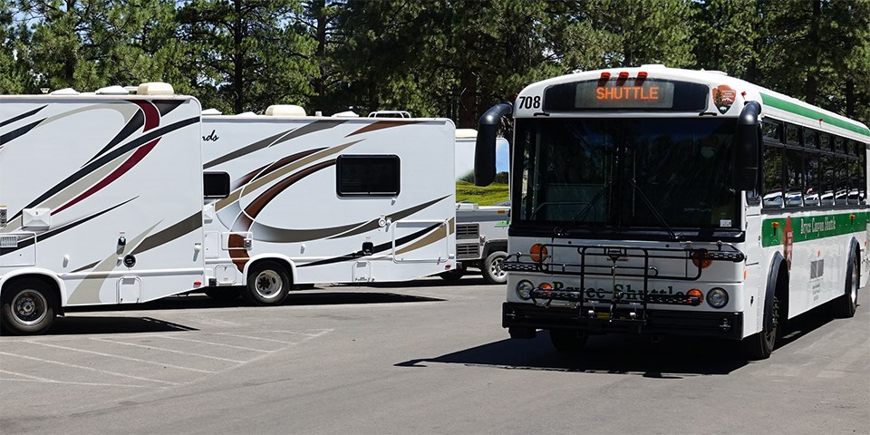 A park shuttle bus drives past multiple long recreation vehicles