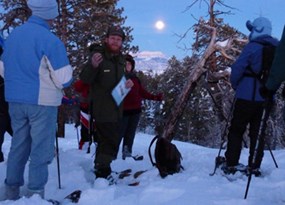 Ranger standing with group on snowshoe with moon rising over distant plateau