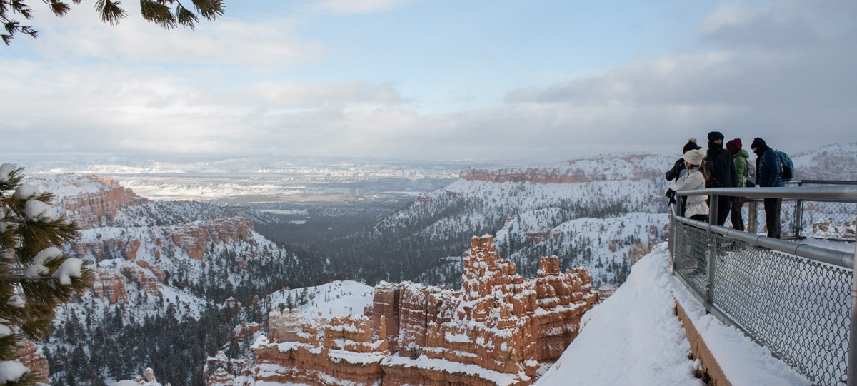 Visitors look out over a snowy amphitheater of red rocks