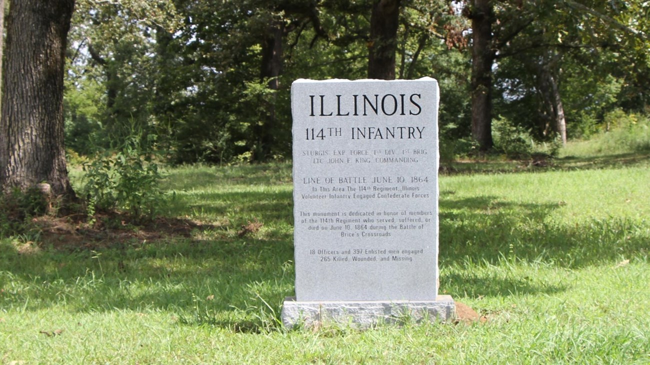 Granite monument in remembrance of the 114th Illinois Infantry who fought at the battle of Brices Cross Roads. Mowed green grass surrounds the granite marker.