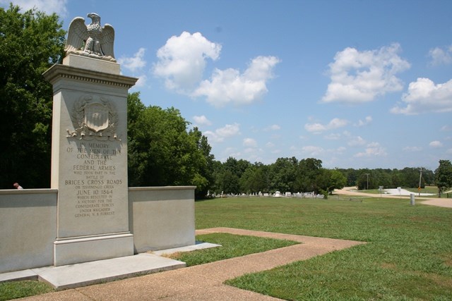 brices cross roads monument in foreground with green grass and roadway in background