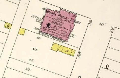 Sanborn Fire Insurance Maps depictive map of the former Monroe Elementary building. There are no cardinal directions on the map. The school building is situated at the top of the center block of three visible city blocks on the map. It rests on a plot of land appearing to be three lots — 505, 507, and 509 — combined and labeled 1501. The building takes up almost the entire width of the three plots, however there are no measurements available on the map. The building is labeled Monroe Public School and Negro in parenthesis, and colored light purple. The front of the building faces the right-hand side of the map. The layout of the building creates a forked or T-shaped hallway, with two large rooms on either side of the entryway. The lower room measures 15 feet in length with no measurement written for width. The upper room measures 12 feet in length with no label for width but is labeled 2B. After the hallway — which is labeled 40 feet — splits directions, there are two more rooms on its far side, neither has measurements. The lower room takes up about two thirds of the rear of the building and has a small black box surrounded by a small outline inside it. Over the floorplan of the building, the following is written Heat – hot air frn system -no lights 15871 degrees symbol C rpsy chem fire extsh on LR FLR bb. On the rear of the building there are two small rectangles attached to the wall with xs drawn from corner to corner, they are labeled Br CHS 10-foot raw eaves.
Next-door to the school, below it in the image is a much smaller building. There are no measurements, but it is colored yellow and marked with a D. This structure is rectangular and sits on a plot of land which consists of lots 511, 512, and 515 — together they are labeled 1507. It rests almost at the top-right corner of the plot. It has four rooms, two large and two small, each room is marked with a one in a top corner and an r in a bottom corner. On the top-left corner of the lot 511 there is a smaller building, colored yellow, marked with a one and an r, which is roughly the size of one of the large rooms from the previous building.
Behind lot 511, across the alley, is another yellow box of approximate size to the last, but with an x drawn from corner to corner. It is labeled one and o.
Next to lot 515, below it on the map, is lot 517. This lot is empty on the map.
The street in front of the Monroe Public School, to its right on the map, is labeled 60 feet and with the letter D. Across the street from the school portions of six lots can be seen on the map, but are empty. These lots are labeled with a large D. The top lot is labeled 1500.
