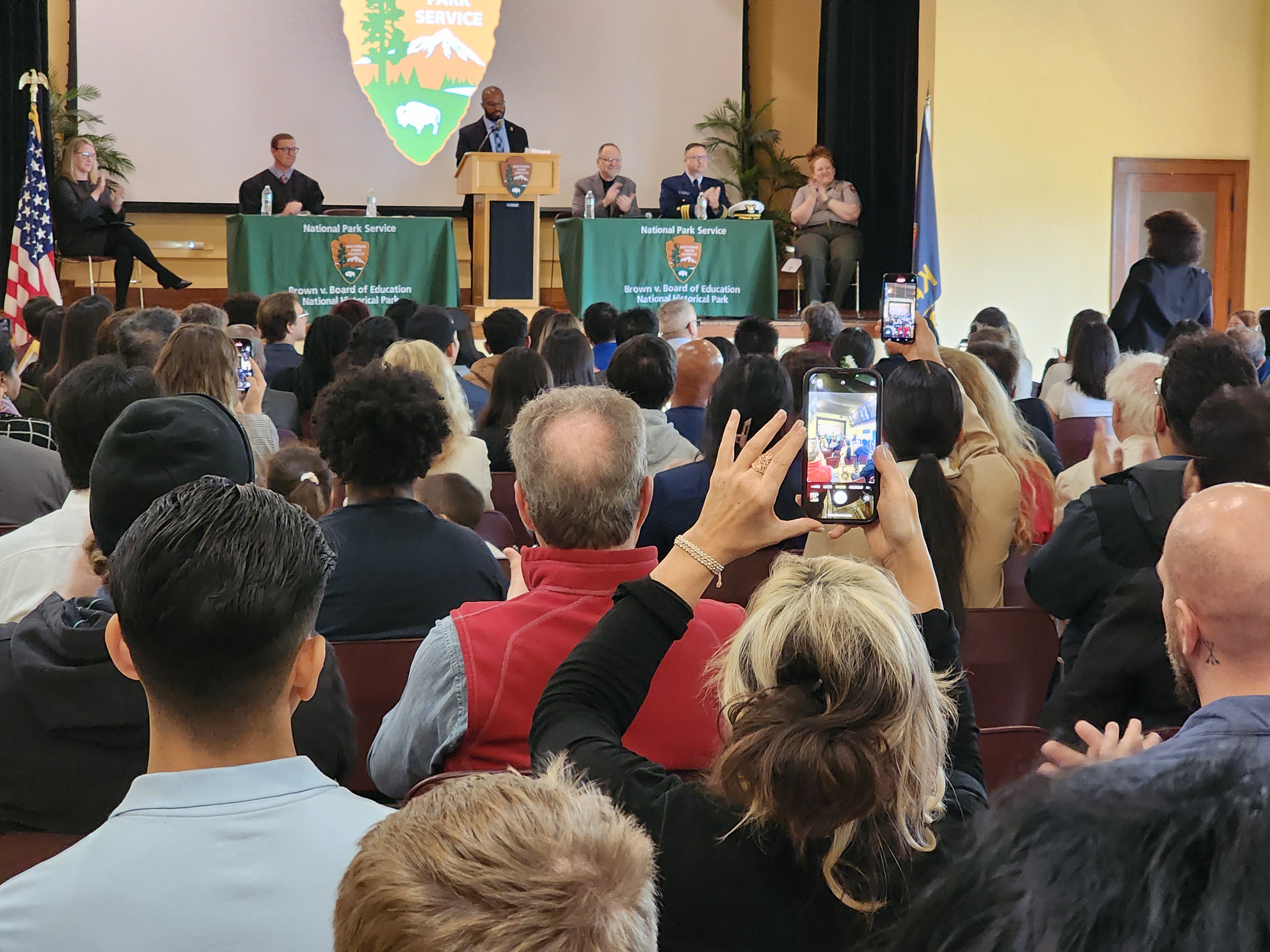 Friends and family take photos with their phones as their loved ones are sworn in as U.S. Citizens.