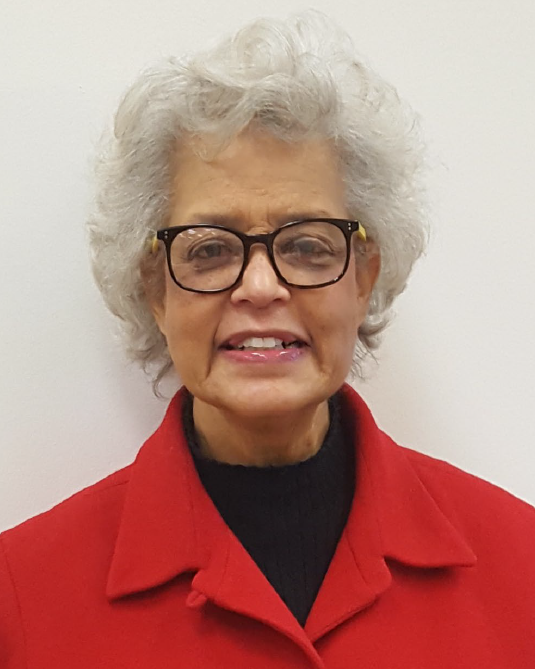 An older mixed-race woman with white hair and black glasses smiles at the camera while wearing a red overcoat.