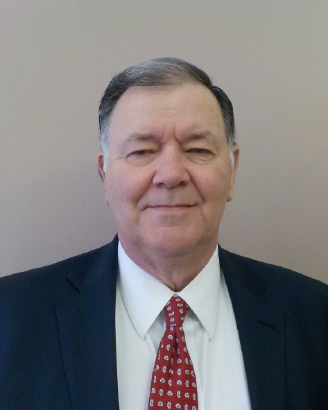 RandySpeaker A older whit man with black and white hair wearing a black suit with white shirt and red tie smiles vaguely