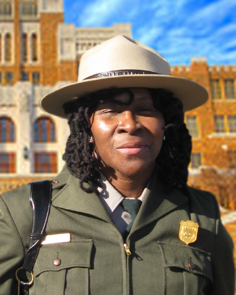 RobinWhite Portrait of a black female park ranger wearing her flat hat, and a green overcoat in front of a brick school building
