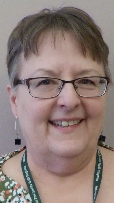 headshot of an older woman with short brown and white hair and purple glasses smiles