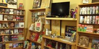 Books and videos on shelves in bookstore. A small television sits on a central bookshelf turned off in front of a yellow wall.