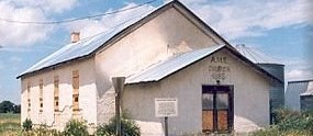 Nicodemus National Historic Site: A whitewashed building with a plaque in front. A grey grain silo is partially visible in the background.