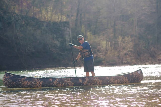A man stands up in his camo canoe as he paddles downriver.