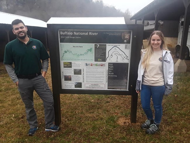Two park volunteers stand by a bulletin board