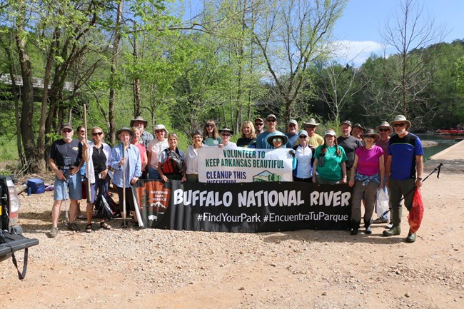 A large group of river cleanup volunteers holds a Buffalo National River banner by the canoe launch at Ponca.