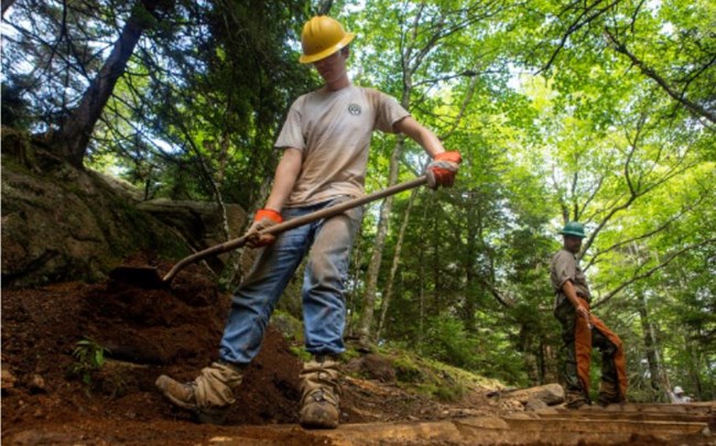 Youth in a hard hat using a shovel on a trail.