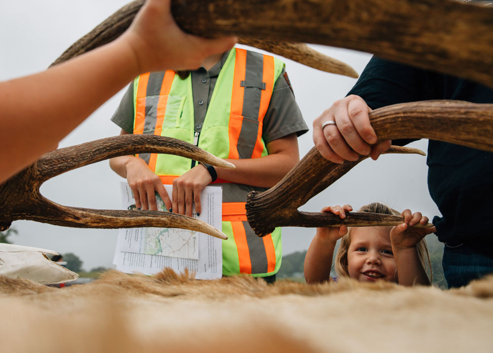 A young girl holds up an elk antler at an educational table. A young girl holds up an elk antler at an educational table.