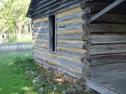 photo of corner of log cabin showing dove tailed logs and daubing covered chinking