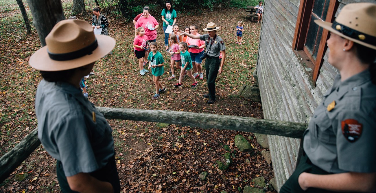 A ranger leading a group of children at a historic site while two other rangers look on.