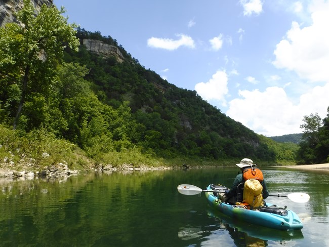 A kayaker paddles away from us on a glassy river