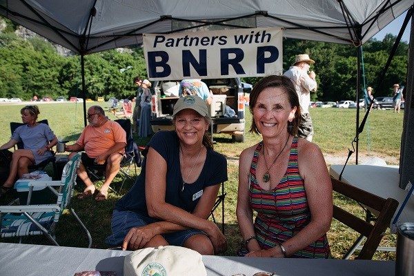 Two women in foreground under tent canopy with BNRP sign in background