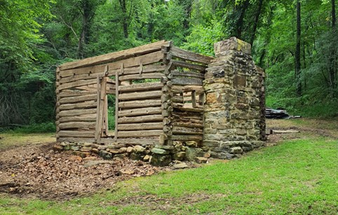 A wooden structure with a stone fireplace surrounded by greenery.