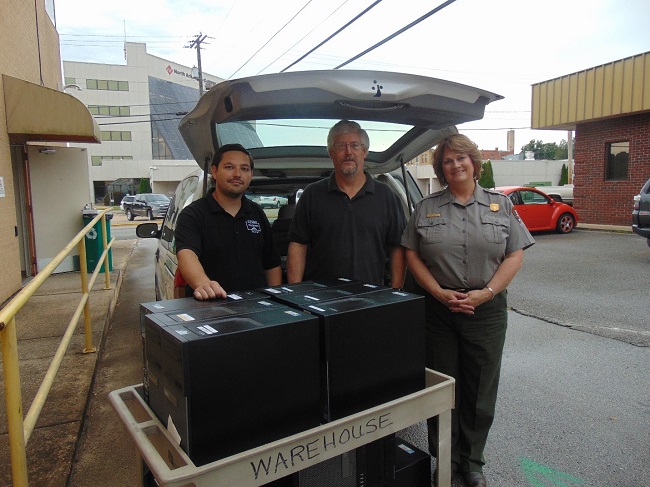 Donated computers 2019 color photo of black computers in foreground and three people in center of photo