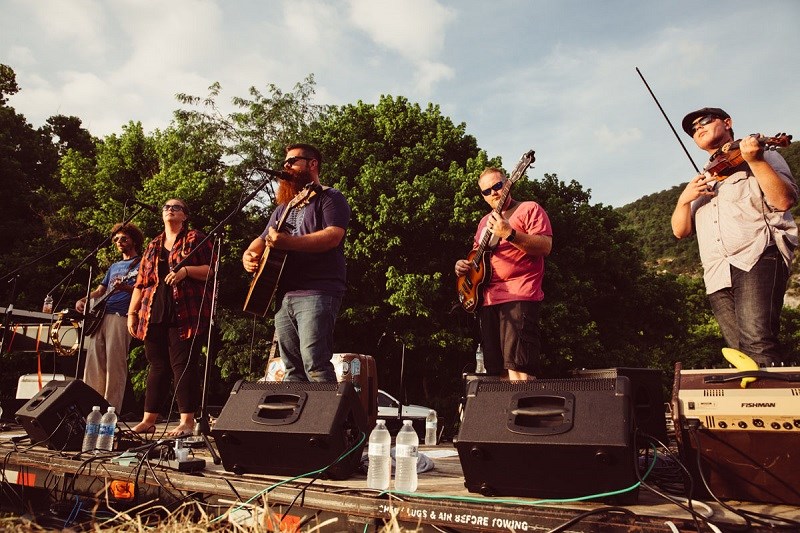 band members playing left to right: guitar, no instrument, guitar, guitar, fiddle