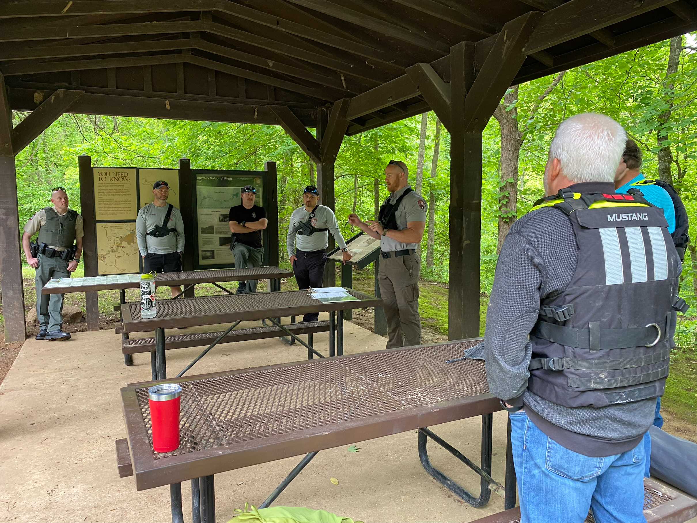 Search and rescue personnel discuss strategy. Color photo of rangers standing around picnic tables.