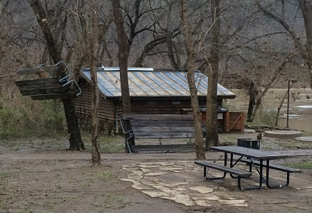 photo showing picnic table hanging in tree near park restroom with flooded river in background