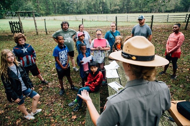 photo of children listening to park ranger (wearing flat hat) at bottom right