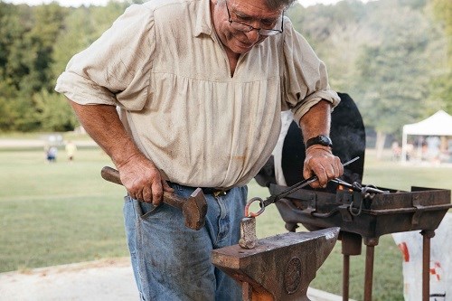 Blacksmith working metal on anvil with forge nearby.