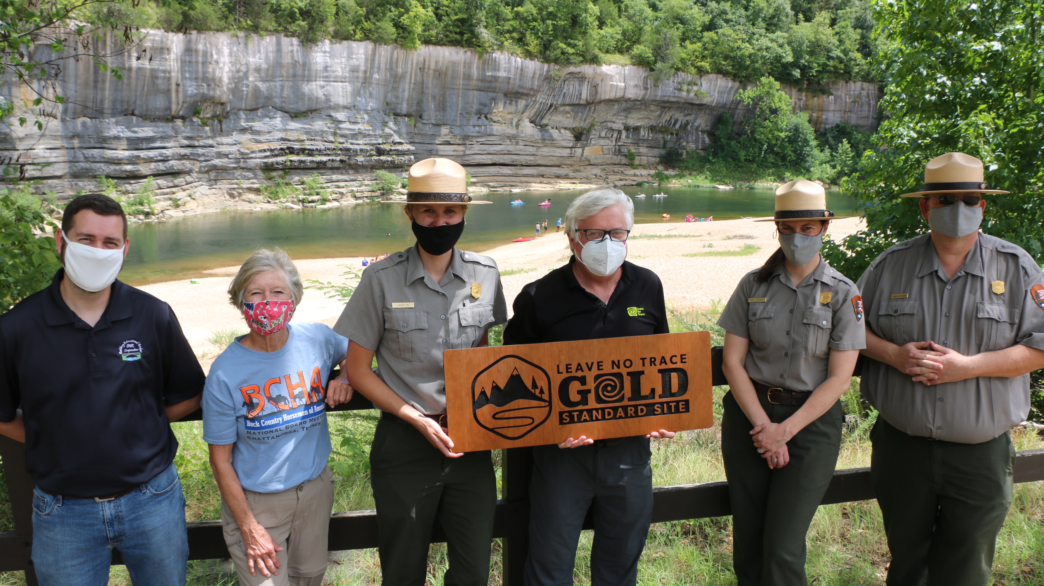 Park Rangers in uniforms and masks are being handed a sign that reads 'leave no trace gold standard' by a group of leave no trace representatives