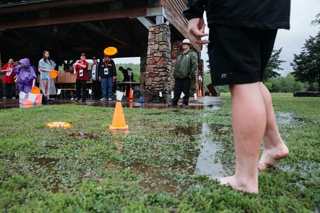 Frisbee golf was part of the Special Olympics Fun Day. volunteers in background, legs of participant right foreground