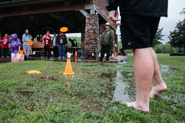 Frisbee golf was part of the Special Olympics Fun Day. volunteers in background, legs of participant right foreground