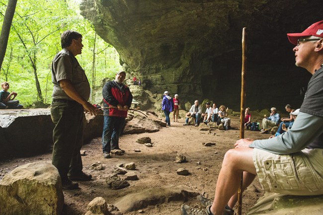 A ranger speaks to a large group of hikers beneath a bluff shelter.
