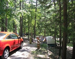 color photo of wooded campsite with red car at left and brown and white tent at right color photo of wooded campsite with red car at left and brown and white tent at right
