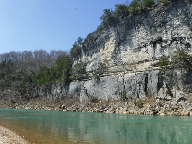Turquoise water flows beneath a stone bluff at Tyler Bend.