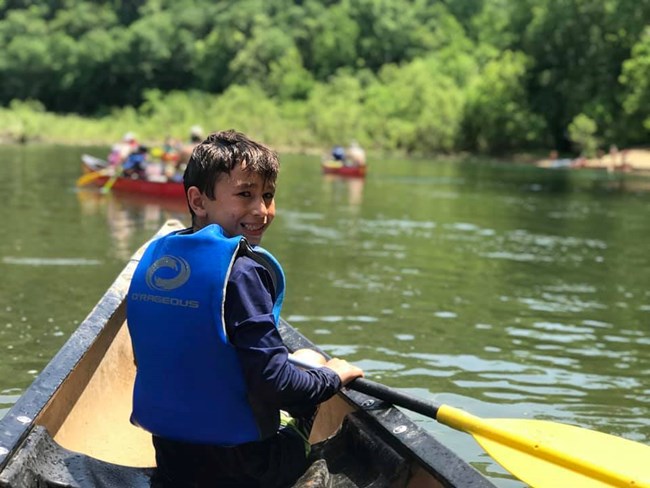 A young paddler in the front of a canoe turns around and smiles at us.