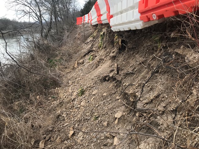 A dirt road crumbles under red and white barriers.