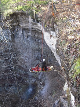 color photo of cliff with waterfall with rescuer on ropes with patient in litter color photo of cliff with waterfall with rescuer on ropes with patient in litter