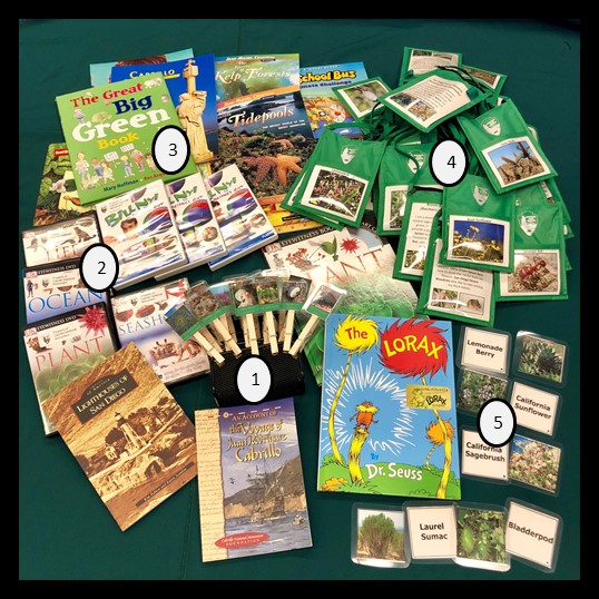 Books, DVDs, and games placed on a table as a display of some of the contents in the Cabrillo Adventure Traveling Trunk.