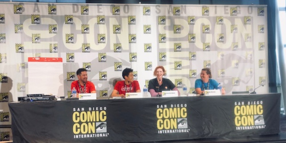 The smiling members of the Conservation + Comics panel sit at a long table draped in black and the SDCCI logo. Samantha Wynns speaks into the microphone.