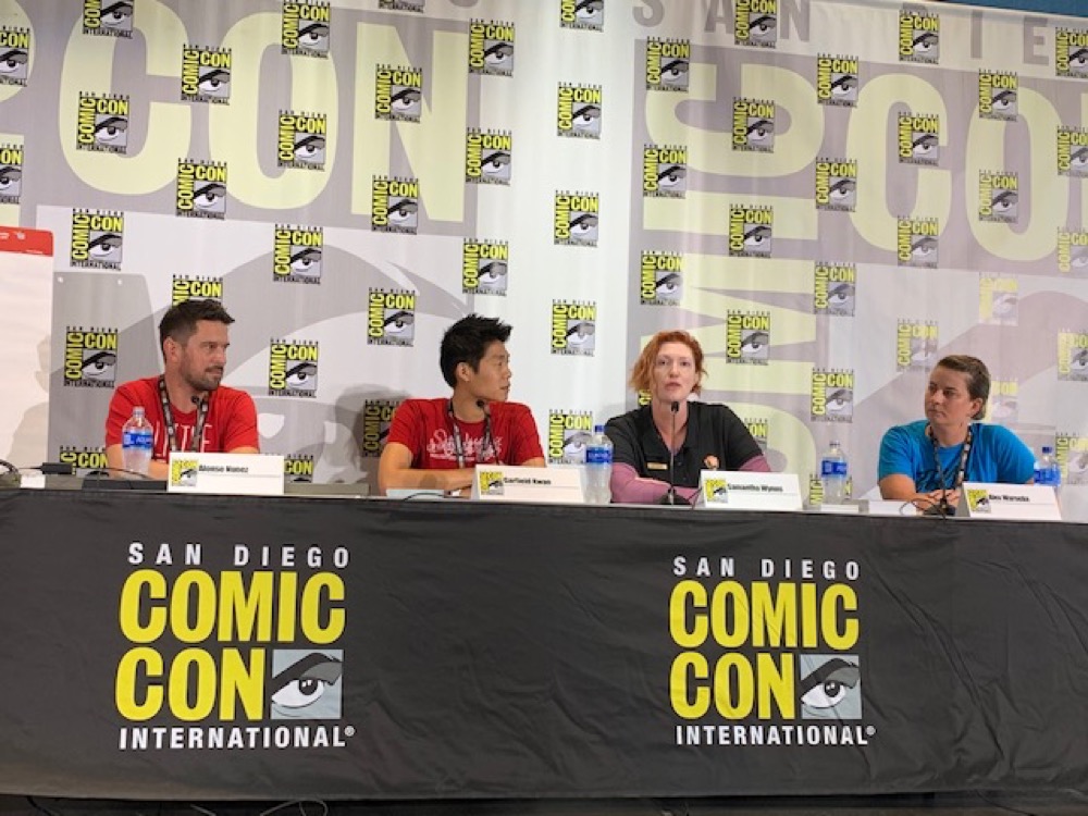 Members of the Conservation + Comics panel sit at a long table draped in black and the SDCCI logo and speak into microphones as they discuss how art is an effective method for science communication.