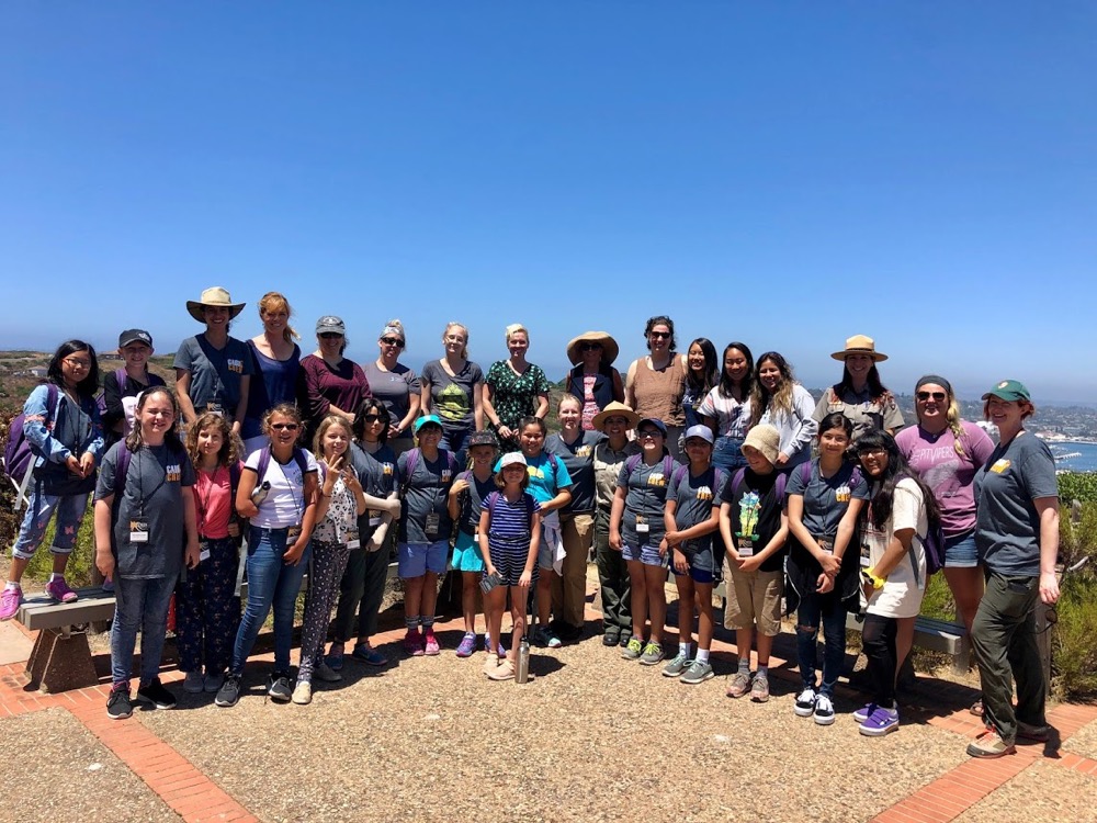 A group photo of female STEM professionals and EcoLogik campers taken during the Women in STEM Fair on the back patio behind the Visitor Center.