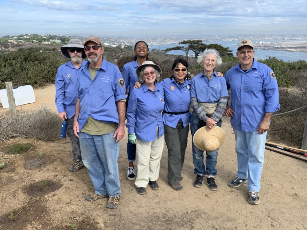 Greenhouse volunteers smile at the camera for a group picture after working together with weed warriors on a large planting project.
