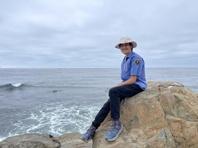 Keanu at the tidepool area sitting on top of a large rock with a small wave crashing to the left in the background.)