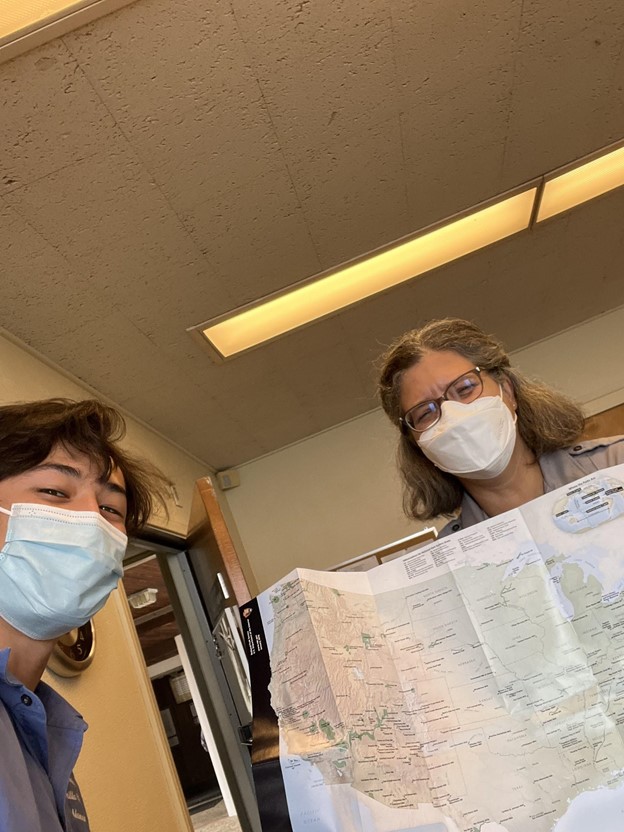Superintendent Andrea holding a map of all national park units alongside intern Keanu in an office