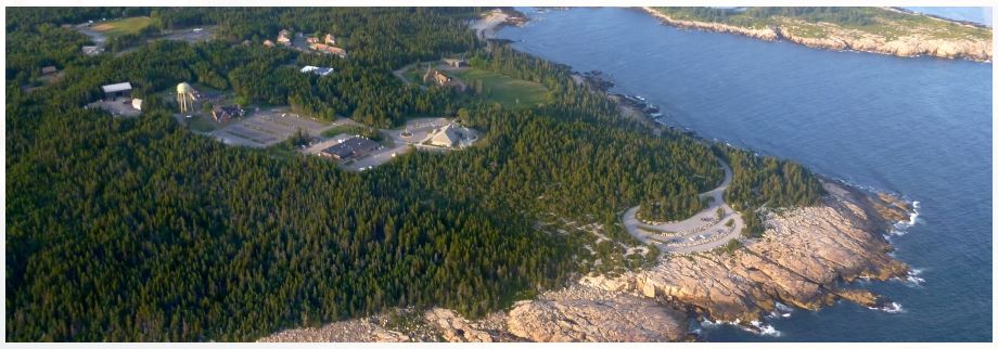 Aerial Photo looking down on Schoodic Point in Maine where the buildings and tree-covered grounds of the Schoodic Institute is located.
