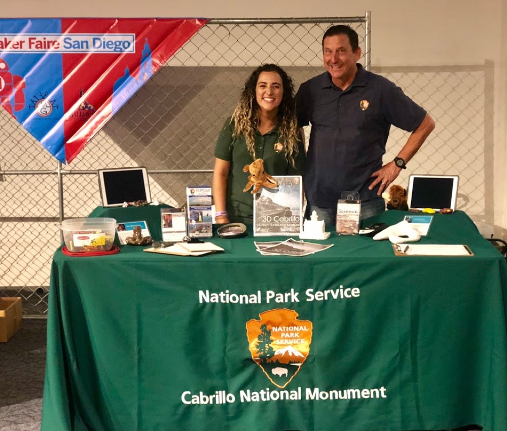 Two Cabrillo Science Education team members smiling for the camera at an exhibit table at the San Diego Maker Faire.