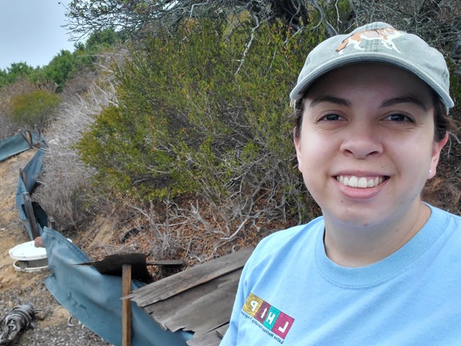 A woman in blue tshirt and baseball cap stands in front of pit array in the field