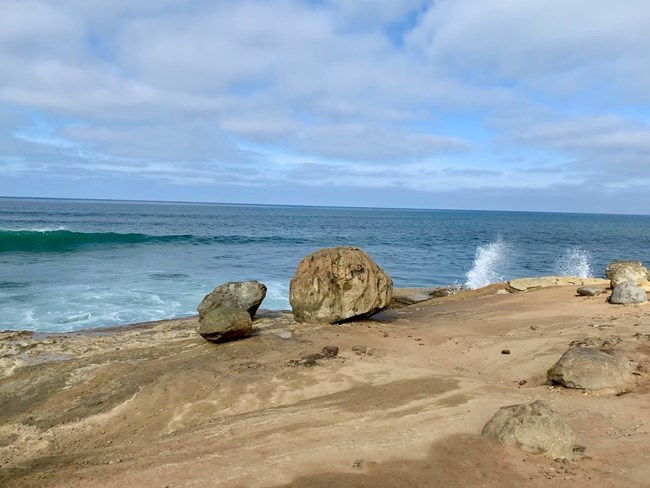 Large boulders, the size of small cars, at the edge of sandstone cliffs overlooking the ocean
